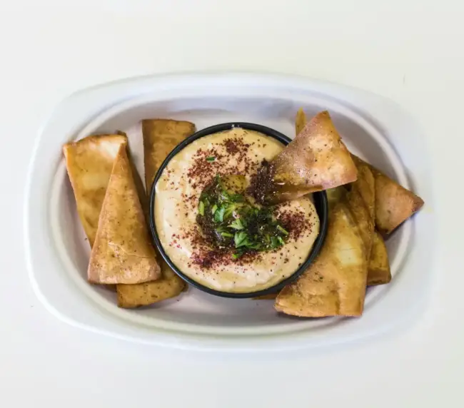 חומוס הבוטקה עם פיתות מטוגנות, תוספות ירוקות ותיבול, מנות מומלצות בגליל.