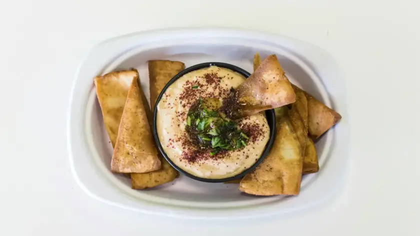 חומוס הבוטקה עם פיתות מטוגנות, תוספות ירוקות ותיבול, מנות מומלצות בגליל.