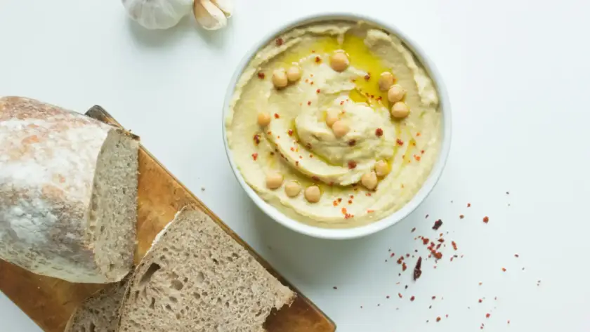 חומוס עבודת יד עם שמן זית וגרגרי חומוס, לצד לחם טרי ושיני שום. חומוס מומלץ!